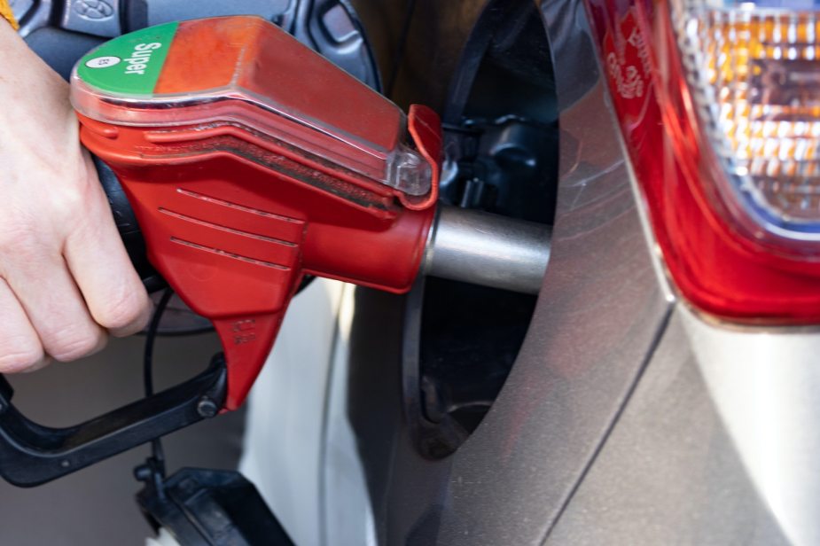 Closeup of a persons hand holding a gasoline nozzle while it pumps gas into their car.