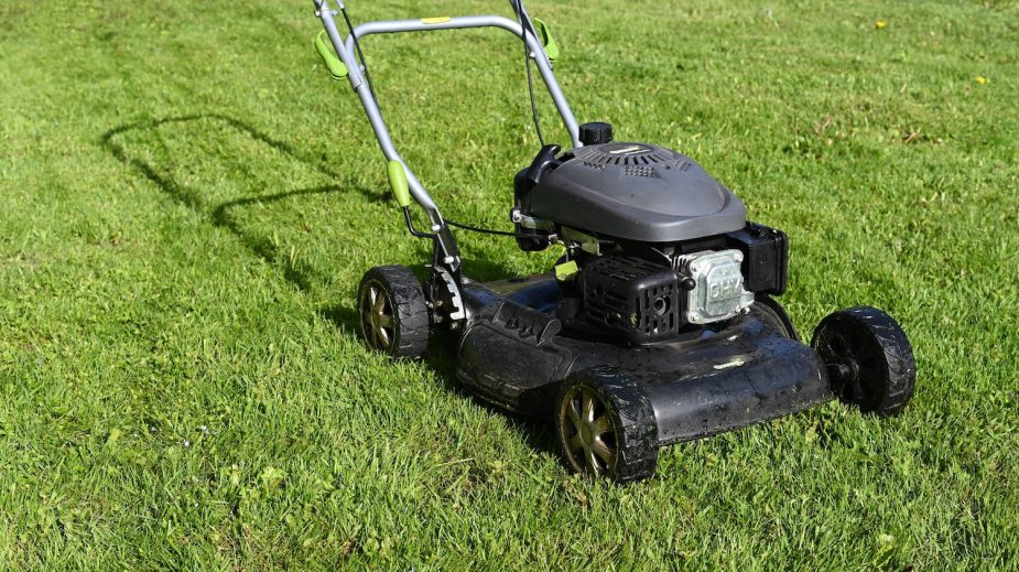 Small, black, walk-behind lawn mower parked on a freshly mowed field of grass.