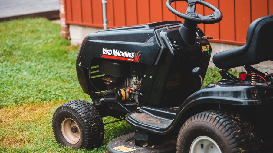Black lawn tractor parked on a yard by a red shed wall.