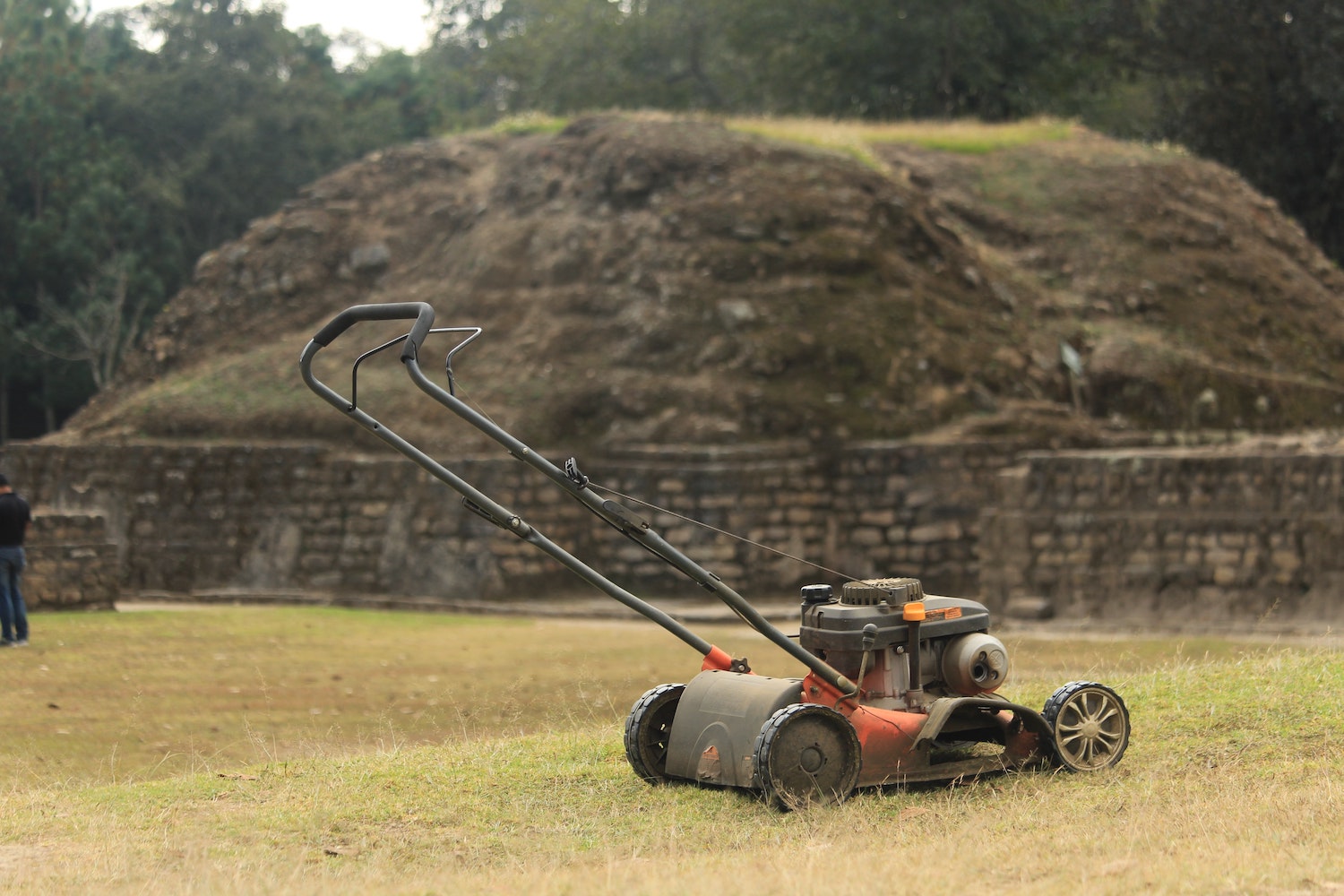 Walk-behind push lawn mower parked in front of a stone retaining wall on a freshly mowed lawn.