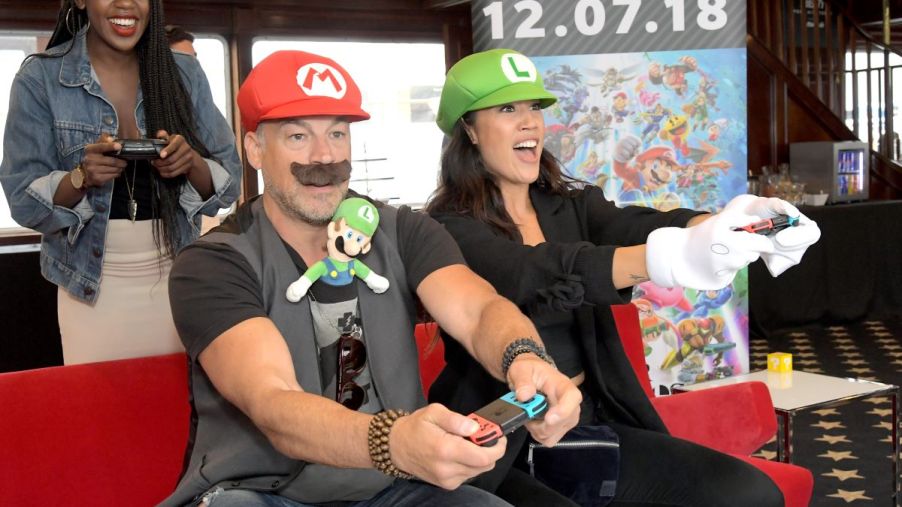 A trio of Mario Kart enthusiasts play the game wearing Mario and Luigi costumes at Comic Con 2018.