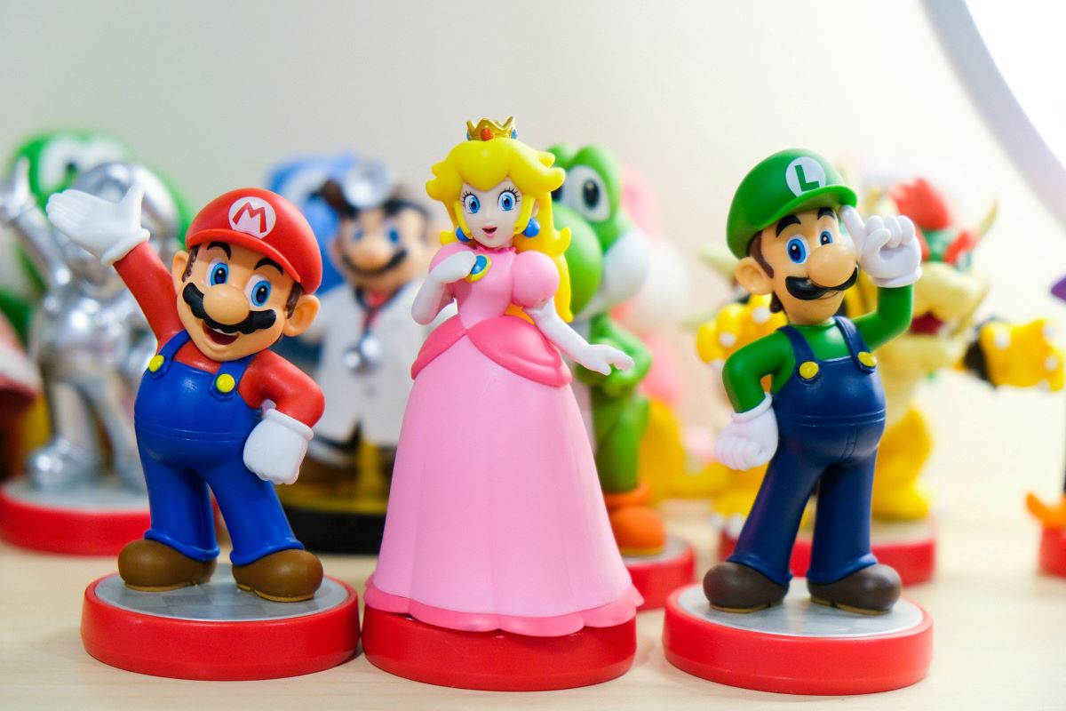 A small figurine of Princess Peach, one of the best female Nintendo characters,  standing in between Mario and Luigi figurines