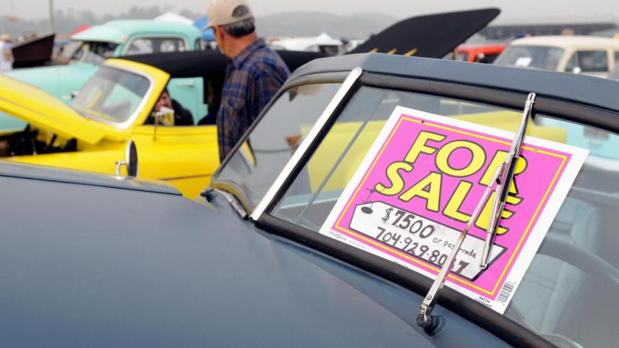 A "for sale" sign is seen on an old classic car.