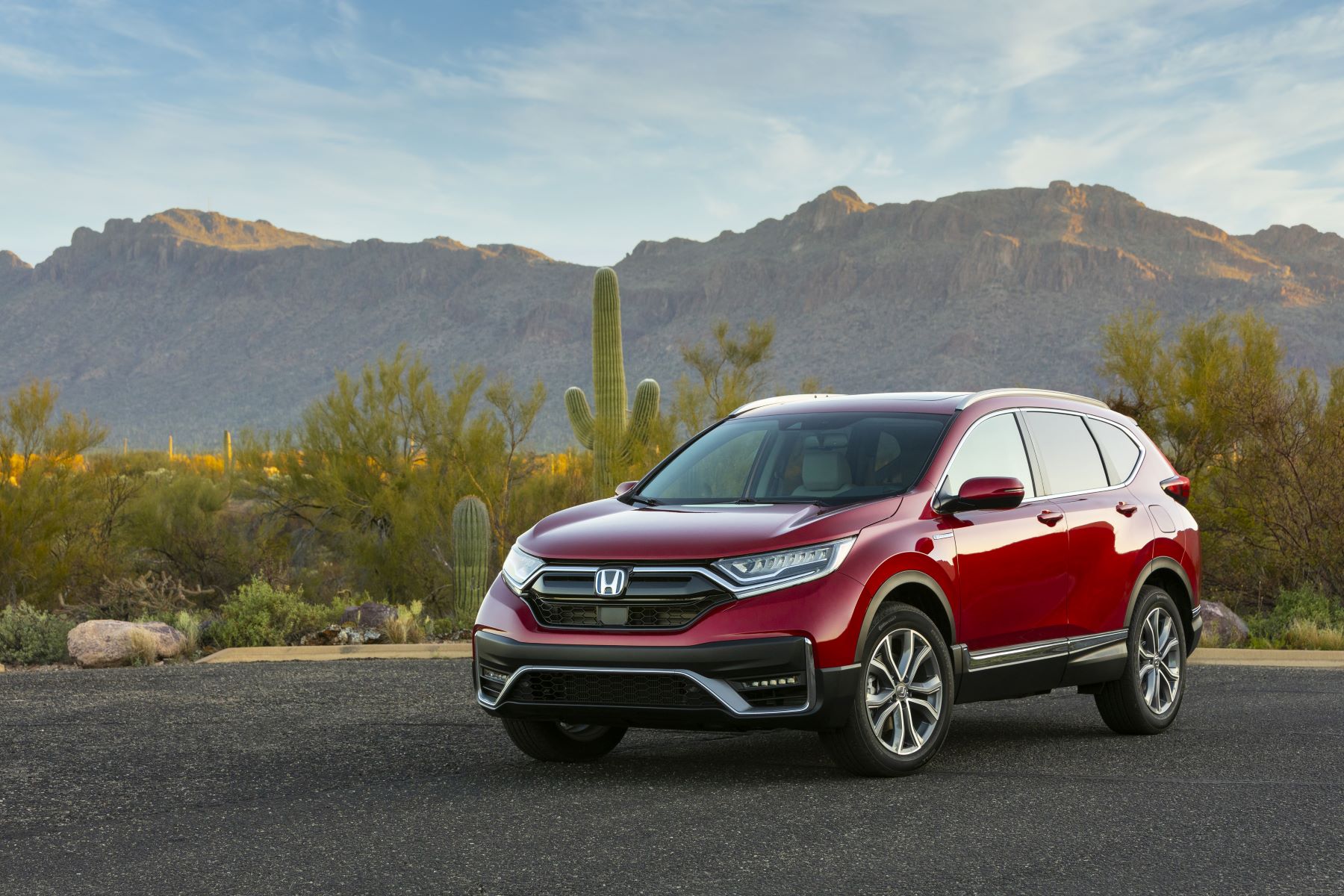 A red 2022 Honda CR-V Hybrid compact SUV model parked on an asphalt lot in the desert near cliffs and cactus