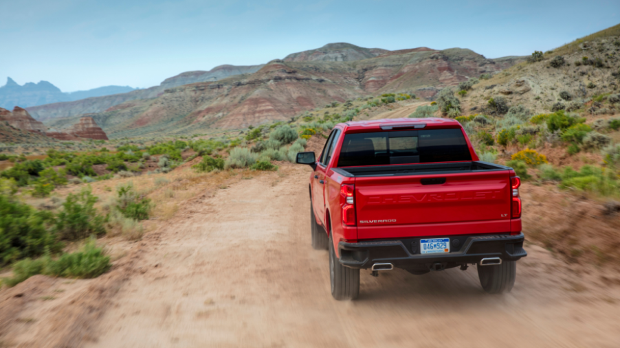 A red Chevy Silverado pickup truck driving on a sandy trail.