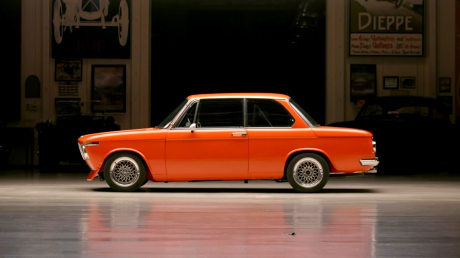 The side view of an orange 1972 BMW 2002 restomod in Jay Leno's garage