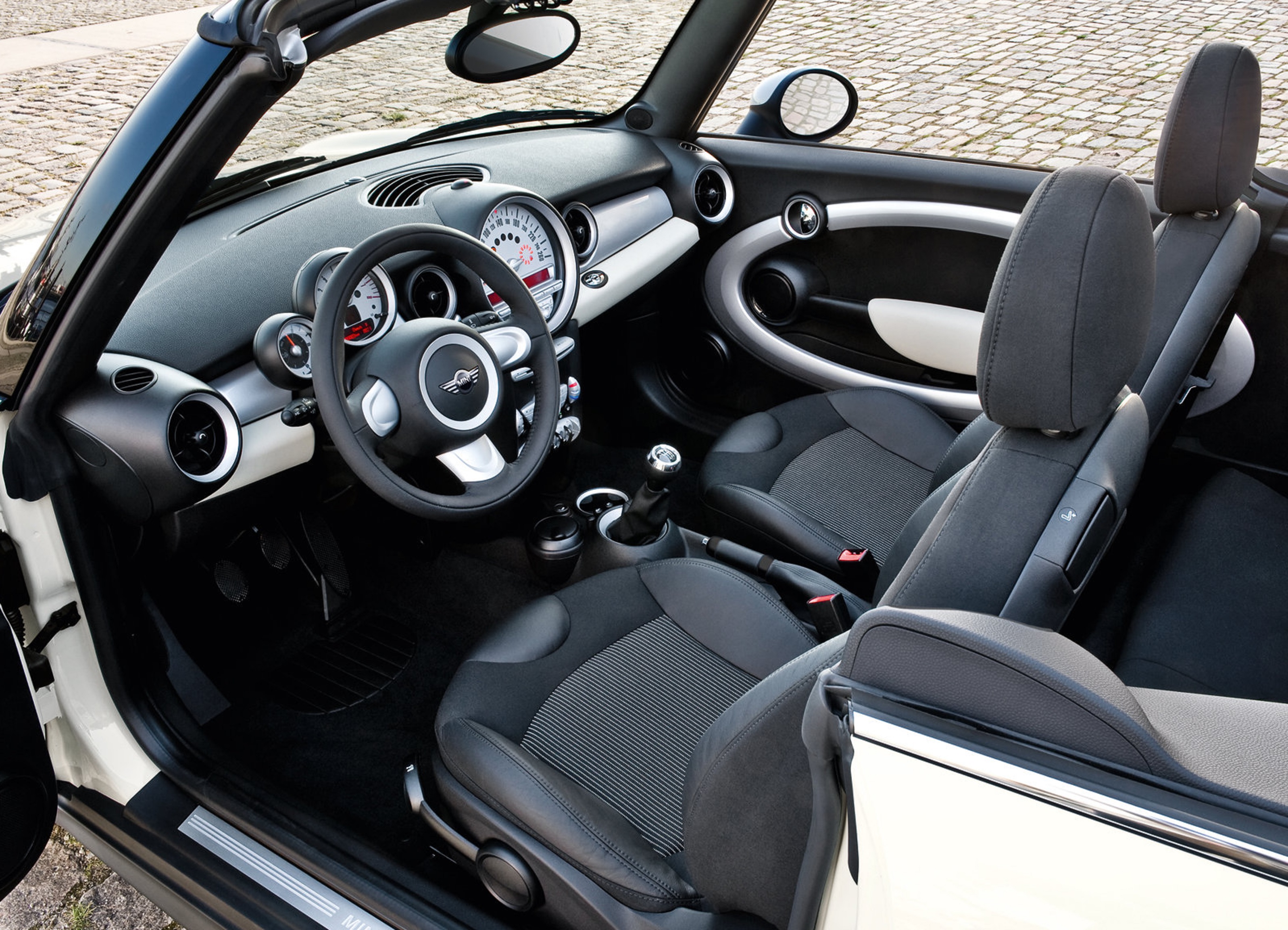 The black seats and black-and-white dashboard of a white 2009 R57 Mini Cooper Convertible