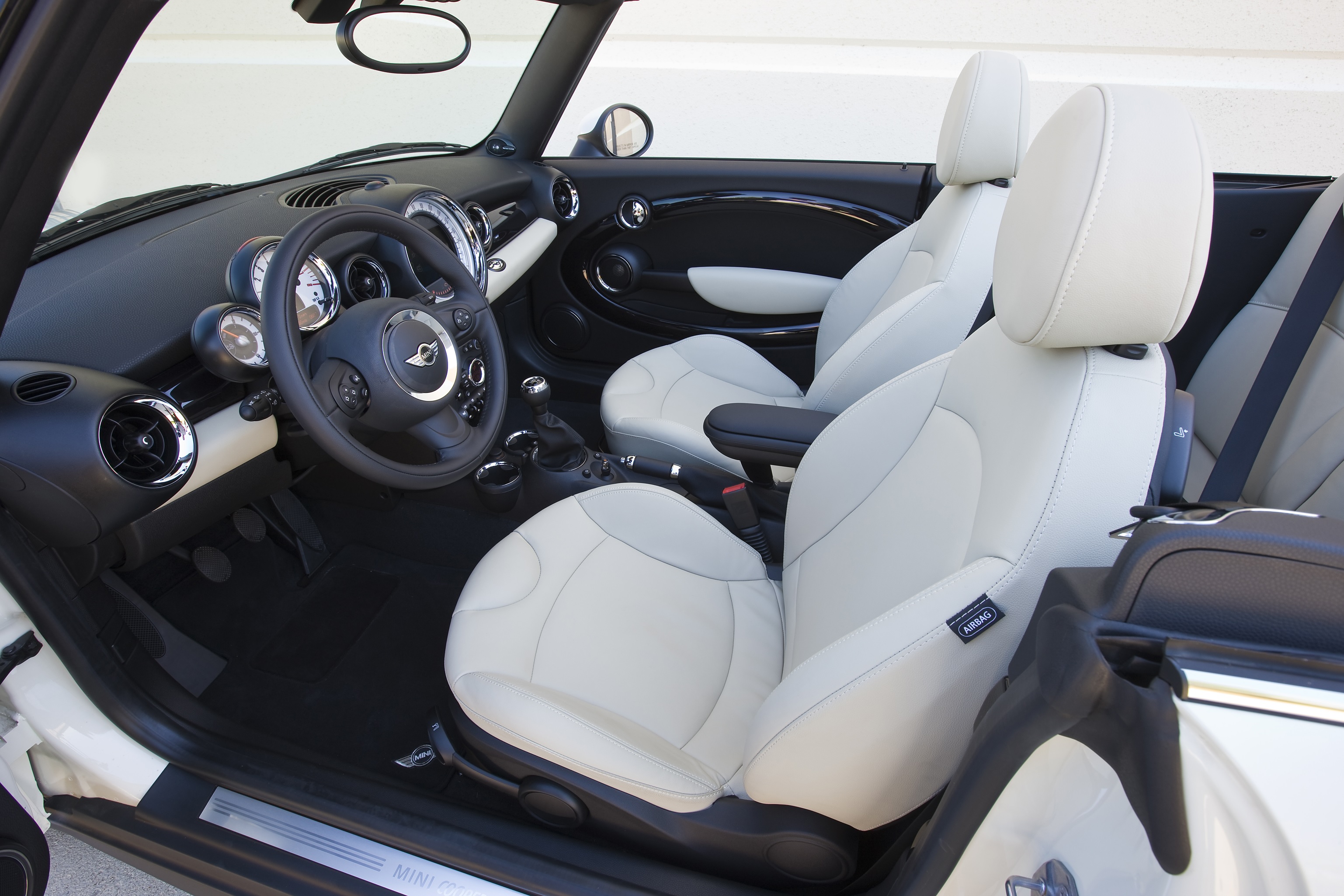 The white-leather seats and black dashboard of a white 2011 R57 Mini Cooper Convertible