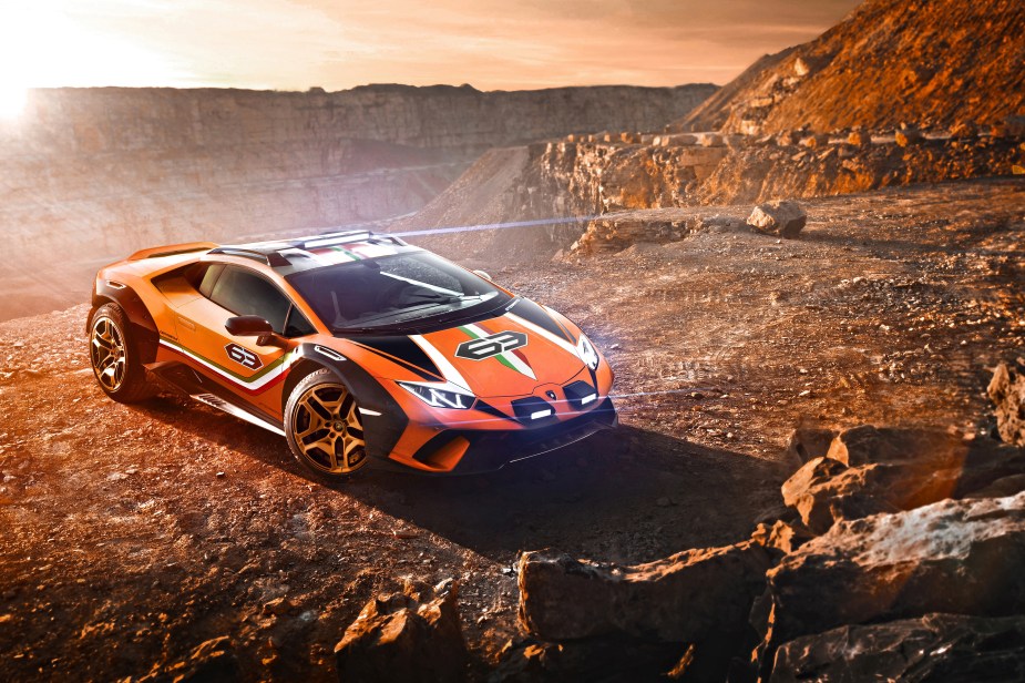 The front 3/4 view of the orange-with-white-and-green-stripes 2019 Lamborghini Huracan Sterrato concept on a rocky mountain