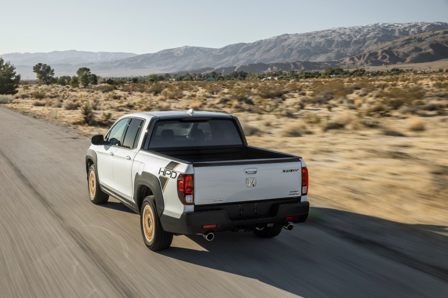 Promo photo of a white Honda Ridgeline pickup truck driving down a desert road, mountains visible in the background.