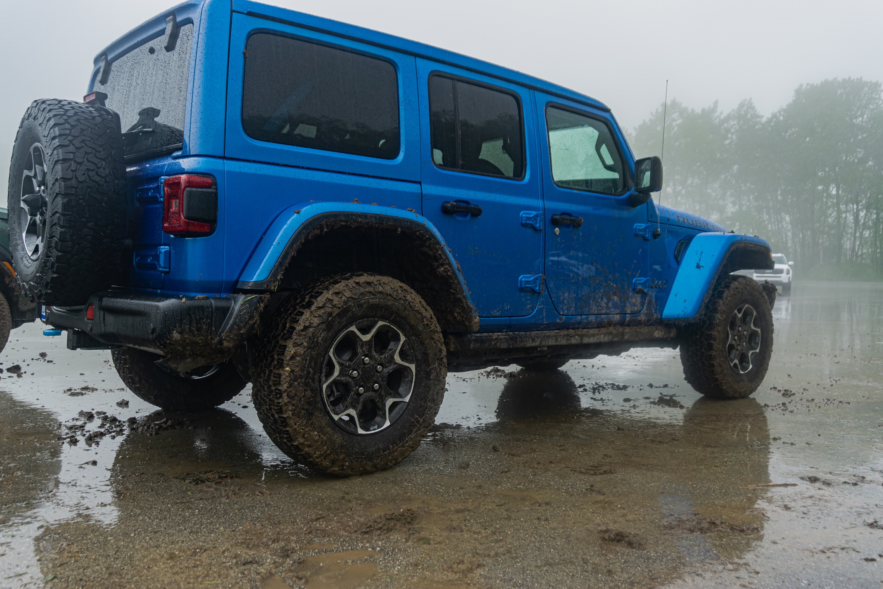 The side 3/4 view of a blue, mud-splattered 2021 Jeep Wrangler Unlimited Rubicon 4xe in a parking lot