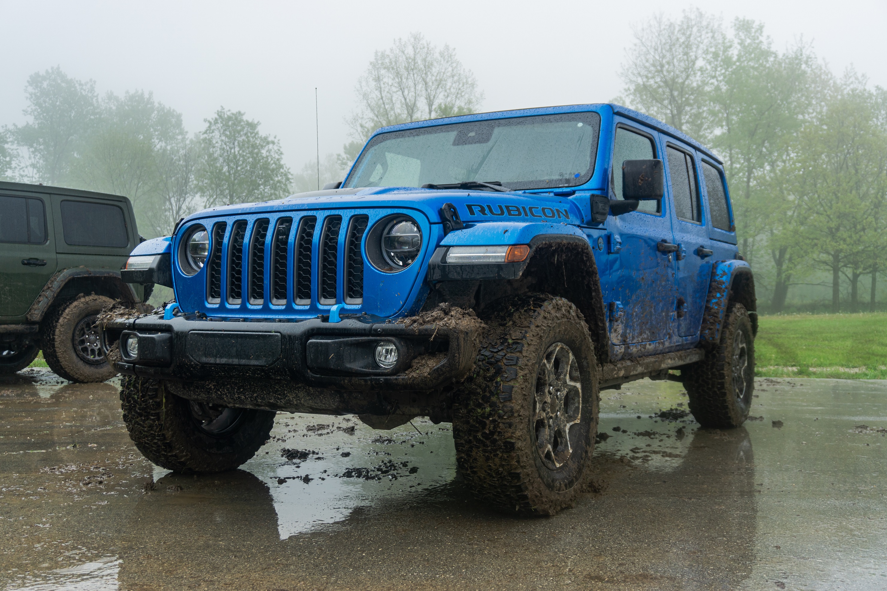 A blue mud-splattered 2021 Jeep Wrangler Unlimited Rubicon 4xe in a forest-side parking lot