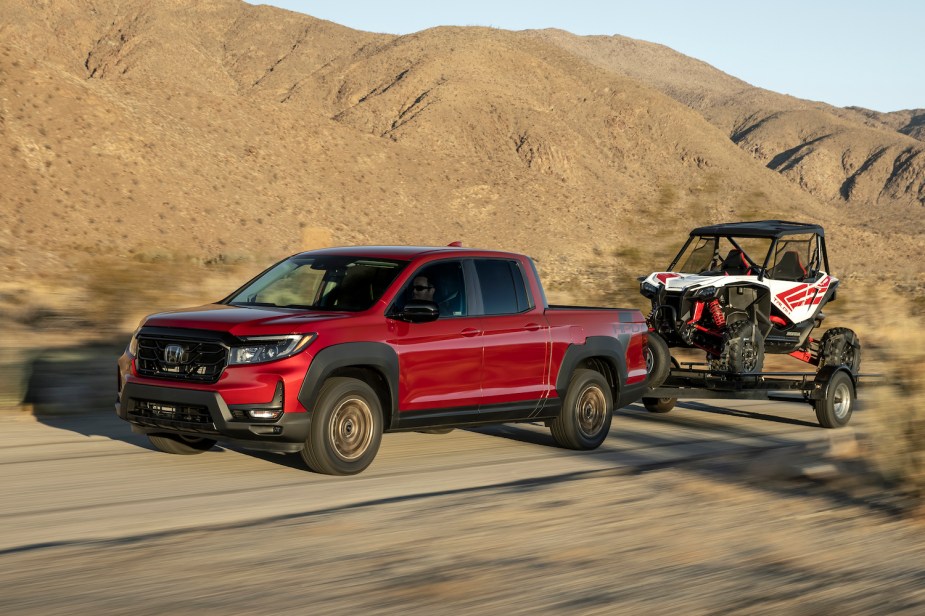 Red Honda Ridgeline pickup truck demonstrating its towing capability while towing in the desert, mountains visible in the background.