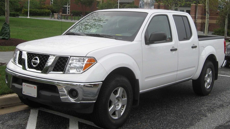 An older Nissan Frontier with a white paint job sits parked on the street.