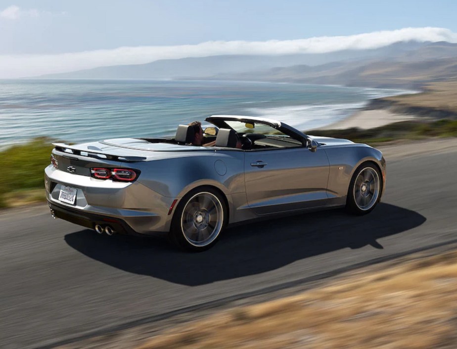 The rear 3/4 view of a silver 2022 Chevrolet Camaro Convertible driving on an oceanside road