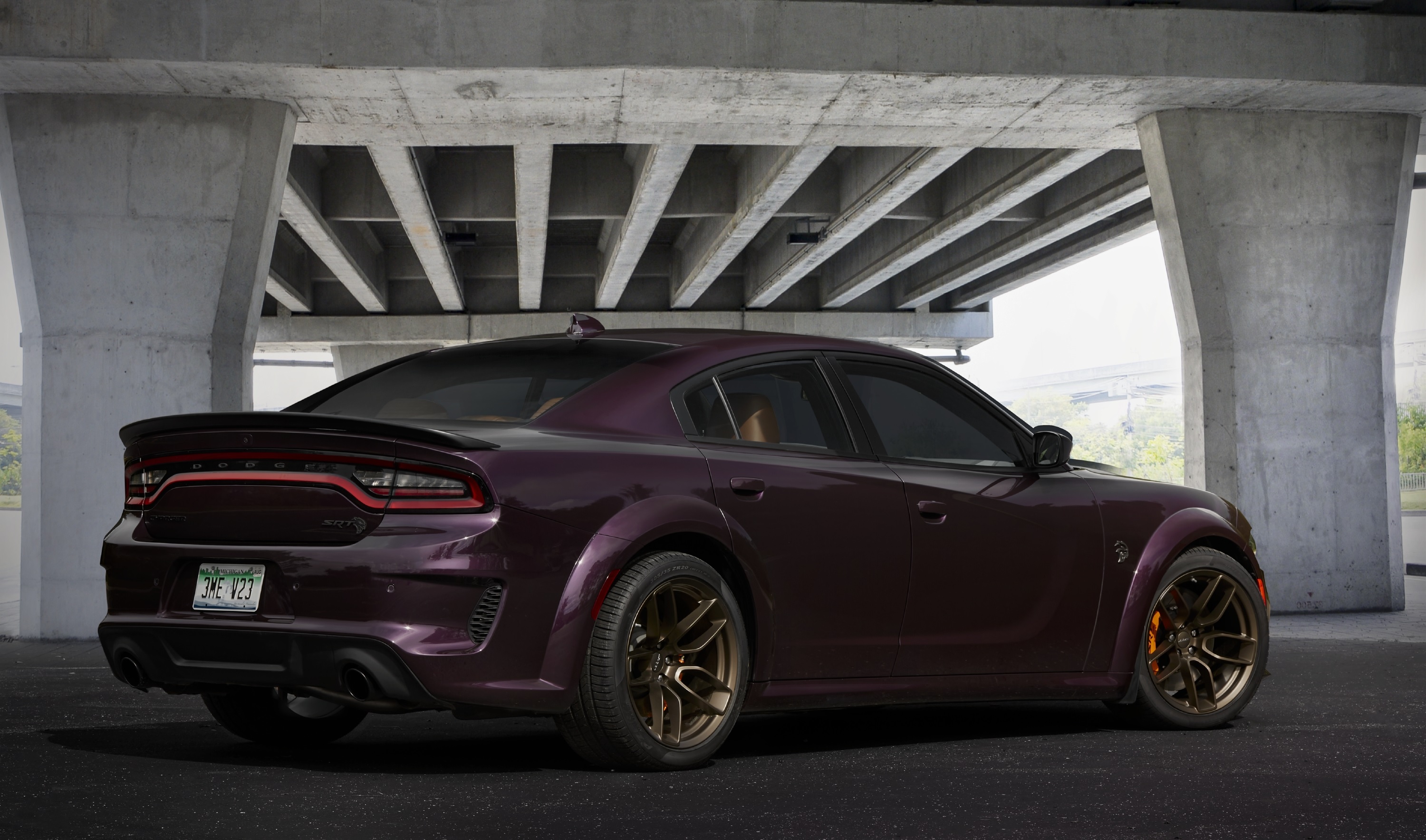 The rear 3/4 view of a purple 2022 Dodge Charger SRT Hellcat Redeye Widebody Jailbreak Edition under a bridge