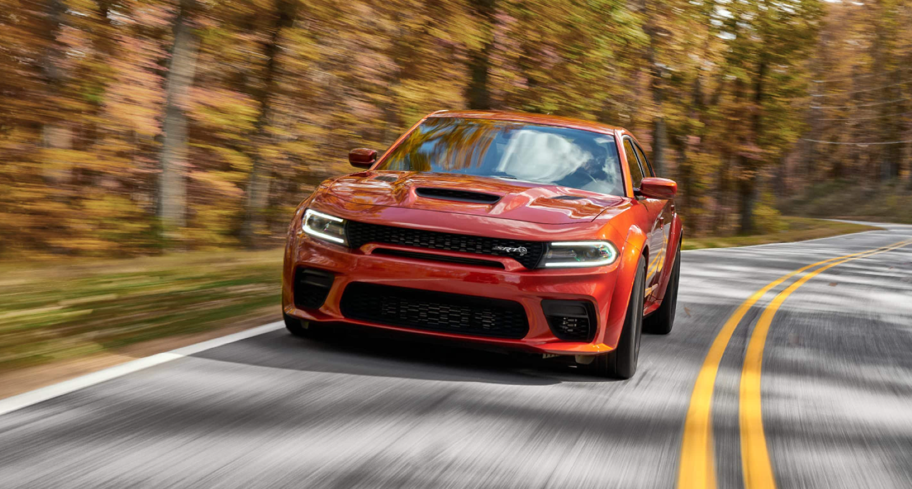 A red 2022 Dodge Charger SRT Hellcat muscle car model driving through an autumn forest