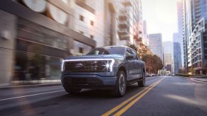 A blue 2022 Ford F-150 Lightning Platinum electric pickup truck driving through a city