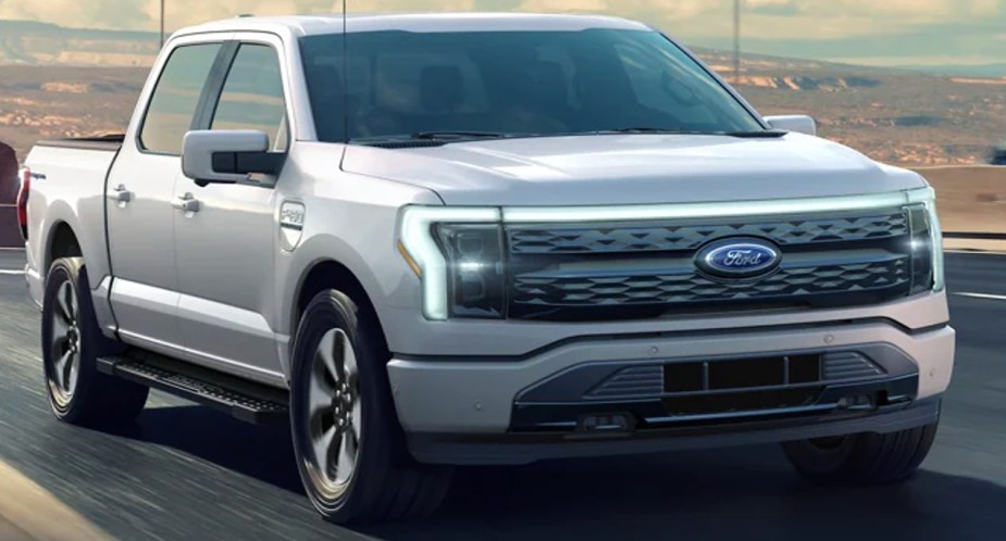 A gray 2022 Ford F-150 lightning is driving on the road. 