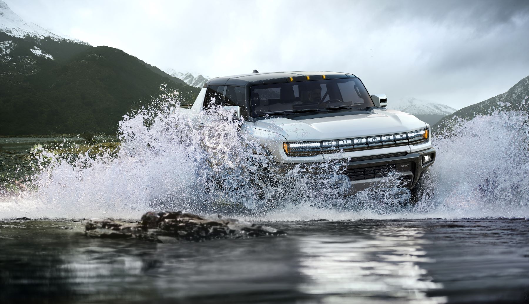 A white 2022 GMC Hummer EV electric pickup truck model driving through a shallow lake