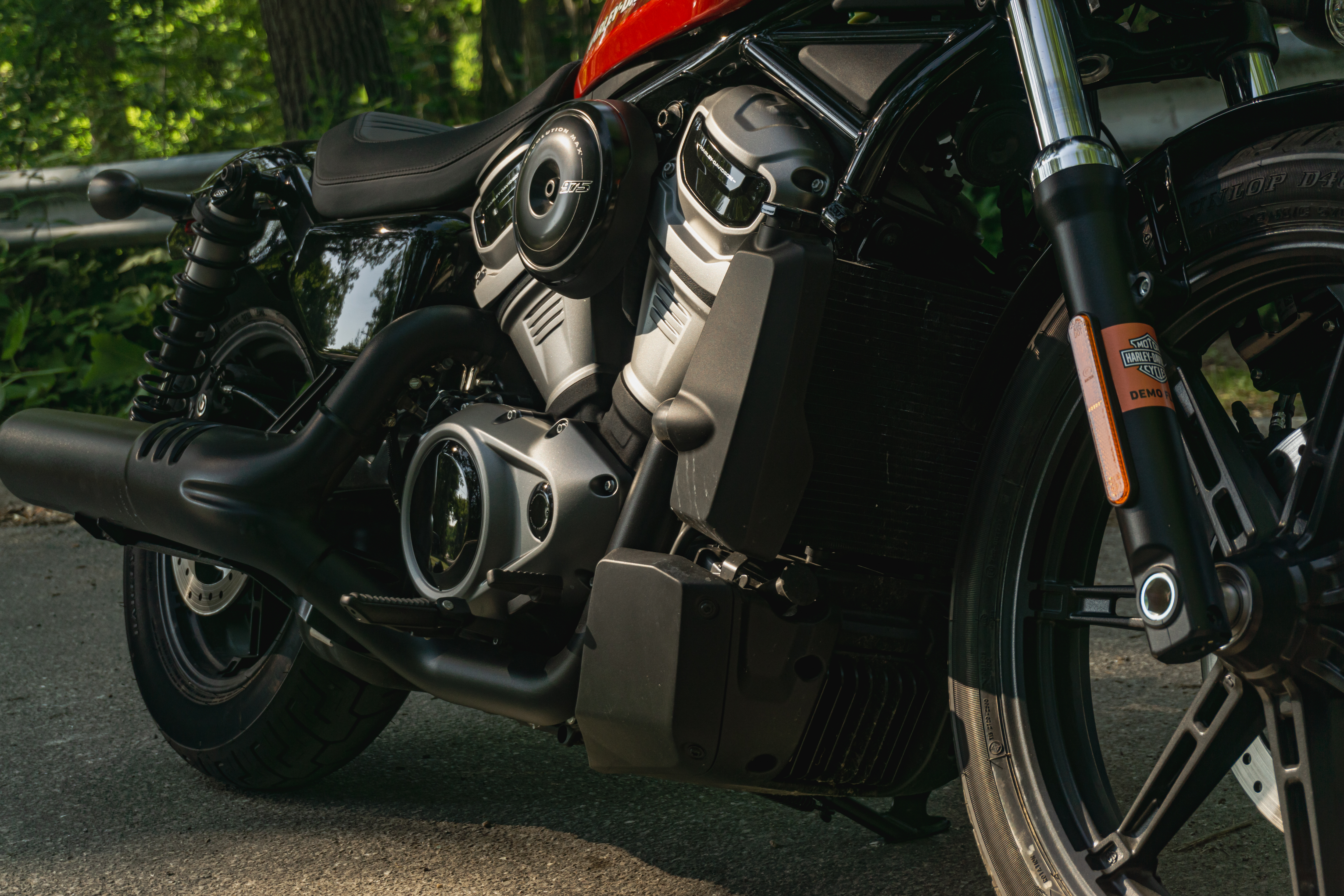 The radiator, engine, and exhaust of a red-and-black 2022 Harley-Davidson Nightster on a forest road