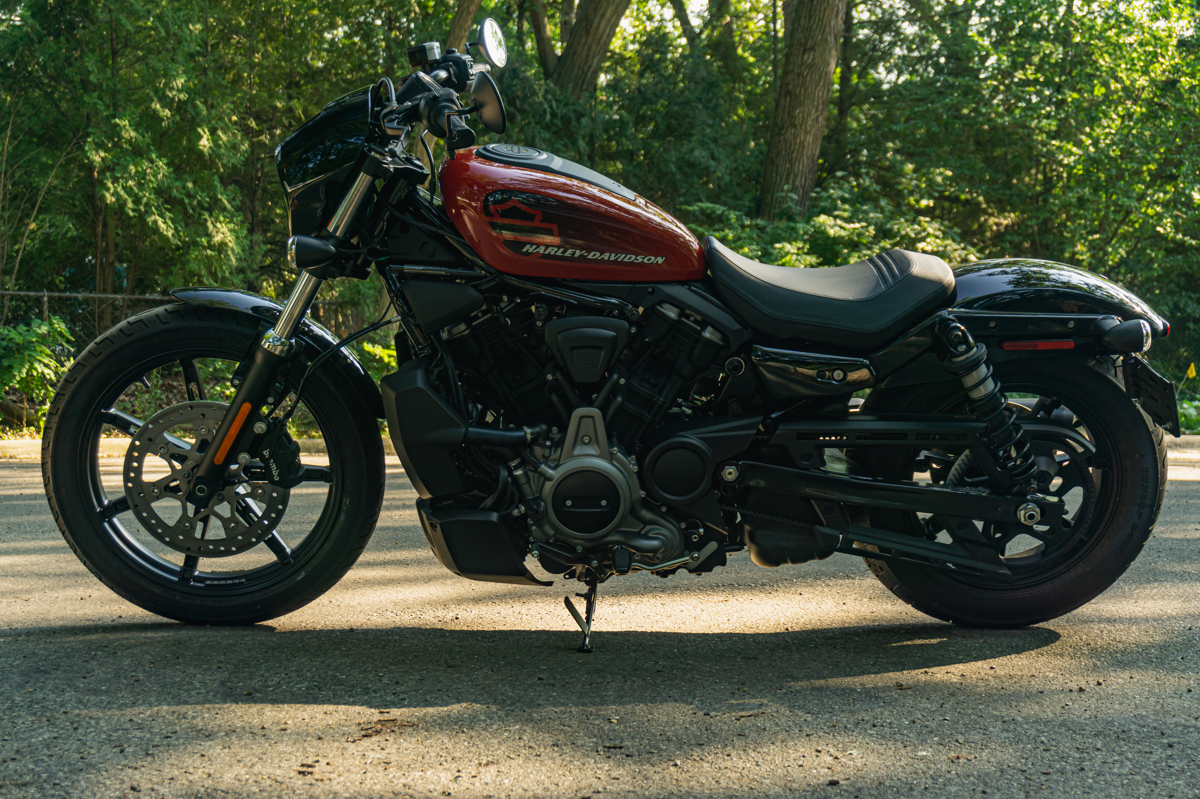 The left side view of a red-and-black 2022 Harley-Davidson Nightster on a forest road
