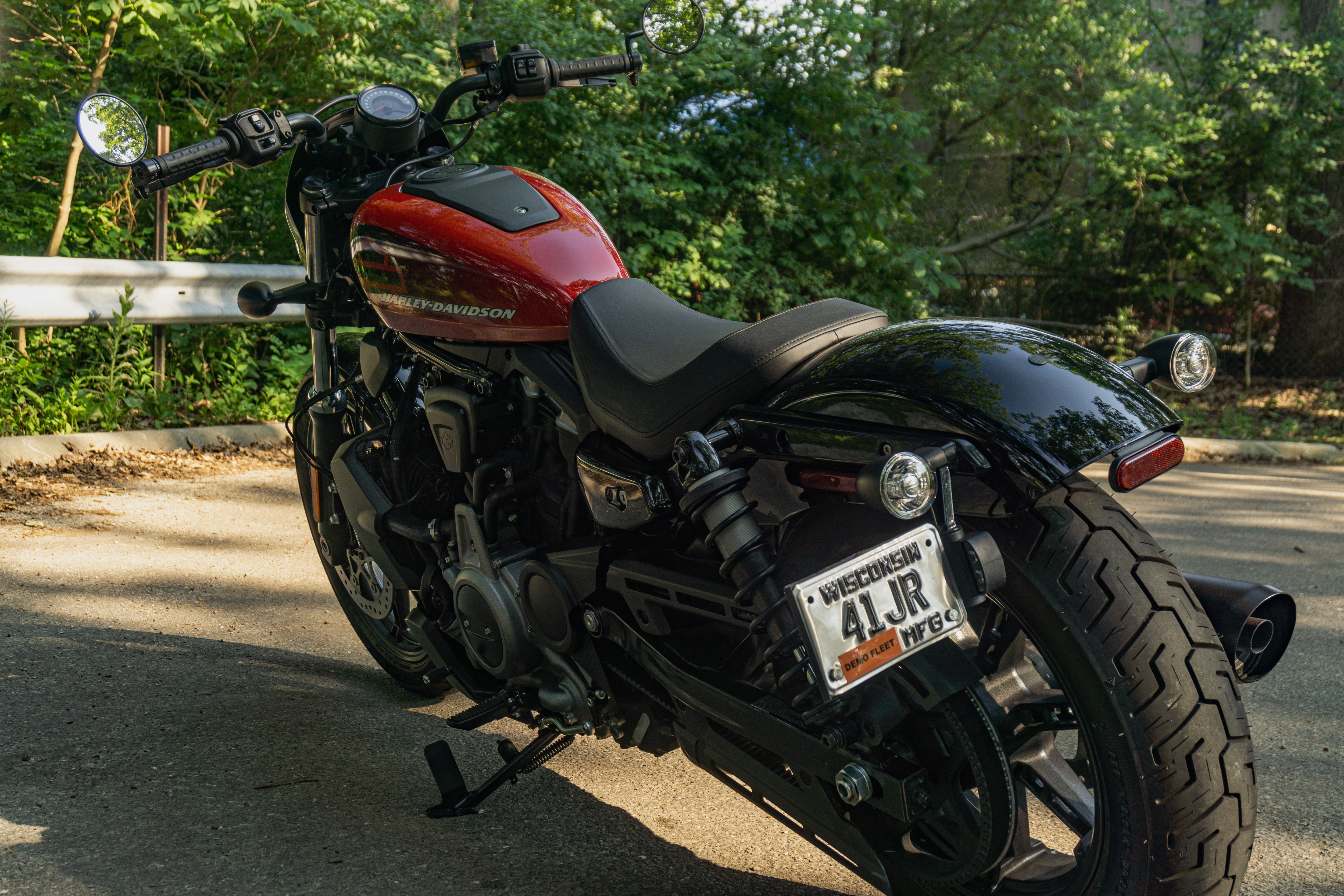 The rear 3/4 view of a red-and-black 2022 Harley-Davidson Nightster on a forest road
