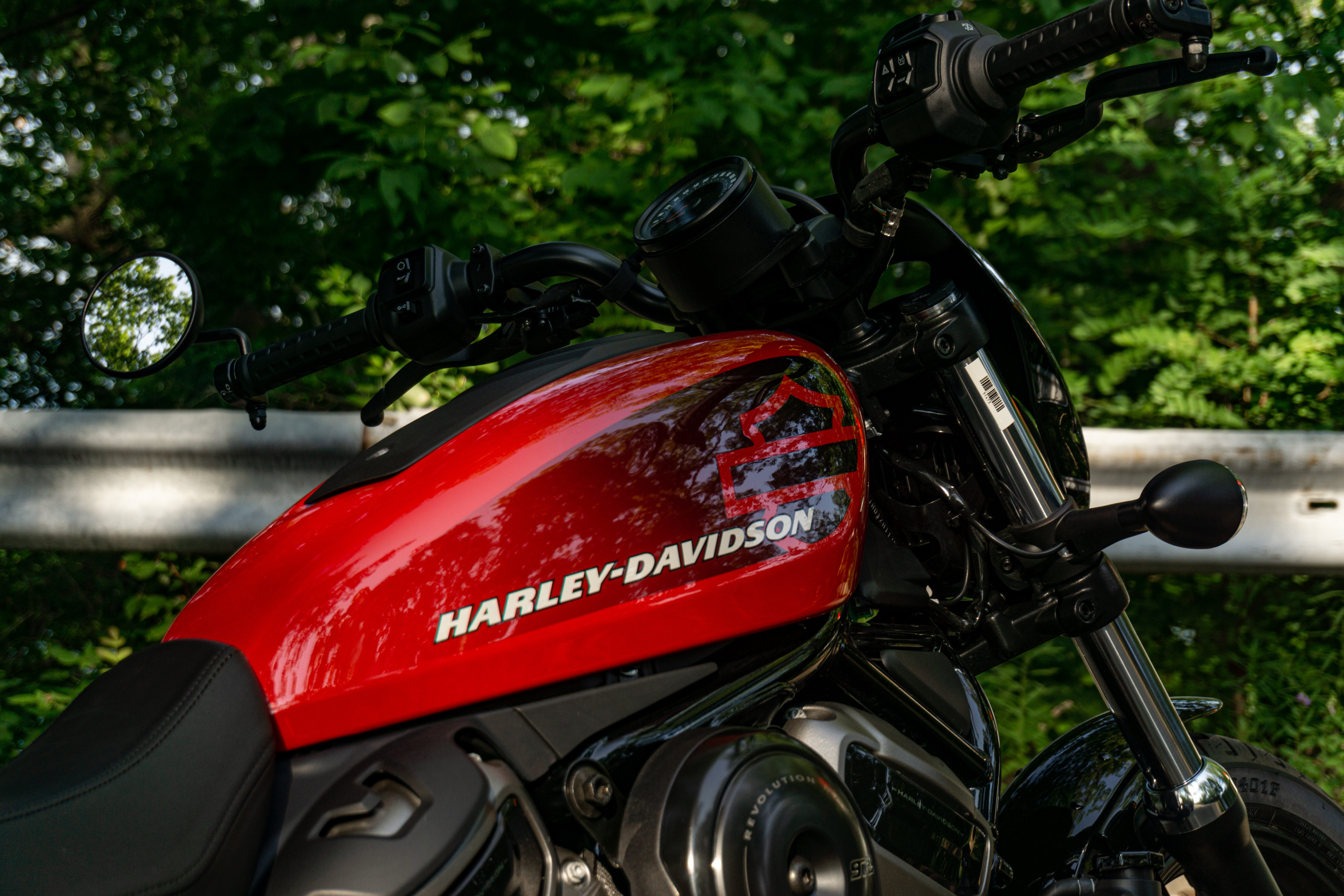 The red tank and black handlebars of a 2022 Harley-Davidson Nightster on a forest road