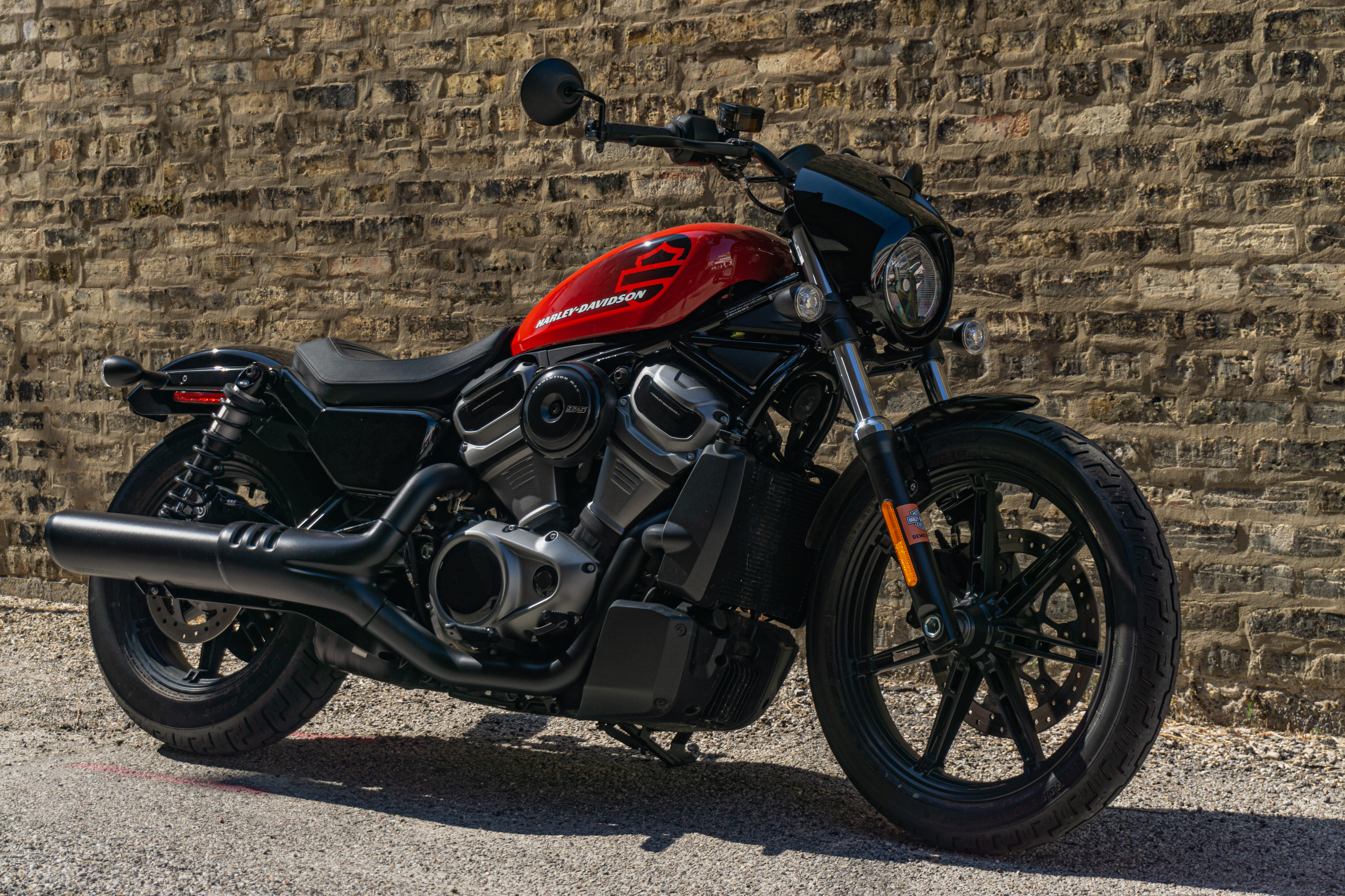 A red-and-black 2022 Harley-Davidson Nightster in front of a brick wall