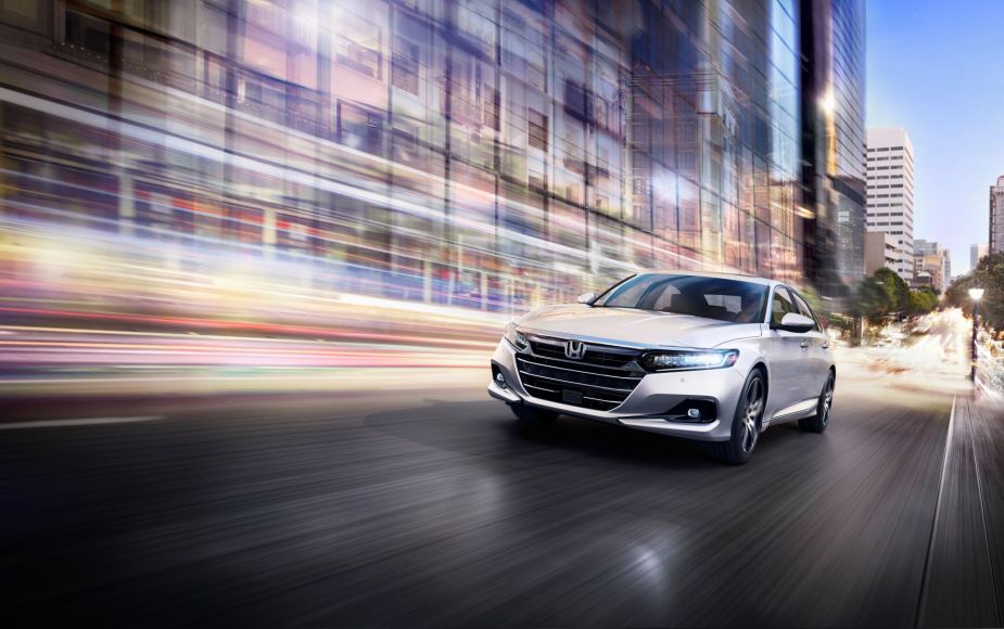 A silver-gray 2022 Honda Accord Touring 2.0T midsize sedan model driving through a city with a background of blurred lighting