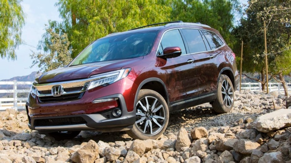 This red 2022 Honda Pilot climbs over some rocks on a trail