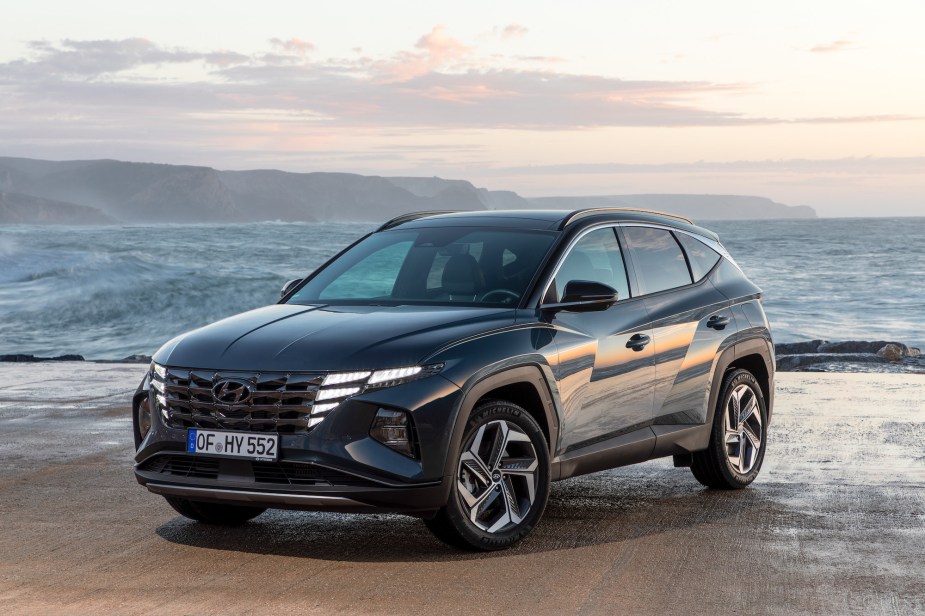 A dark colored 2022 Hyundai Tucson, a compact SUV, parked in front of an ocean scene.