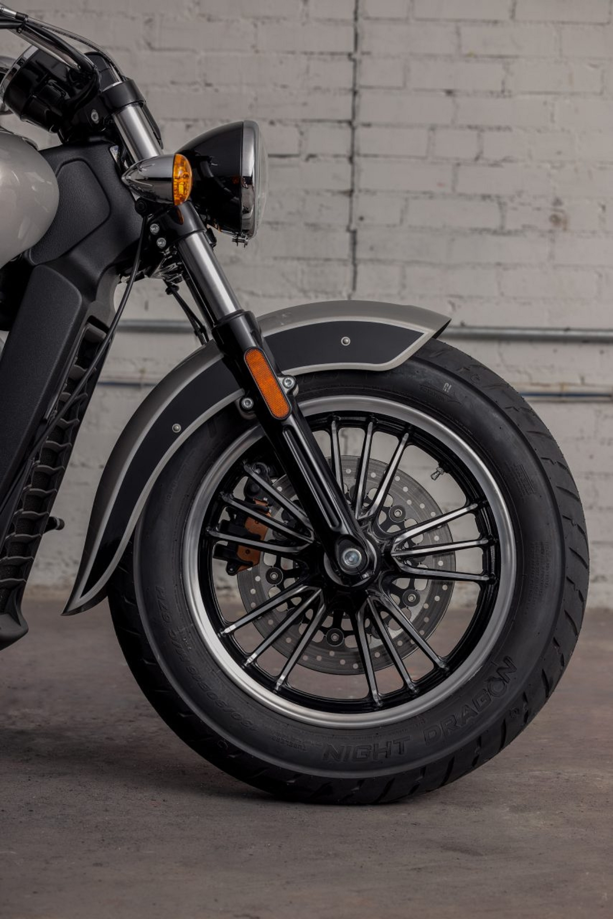 The front wheel and fork of a gray-and-black 2022 Indian Scout in a white storehouse