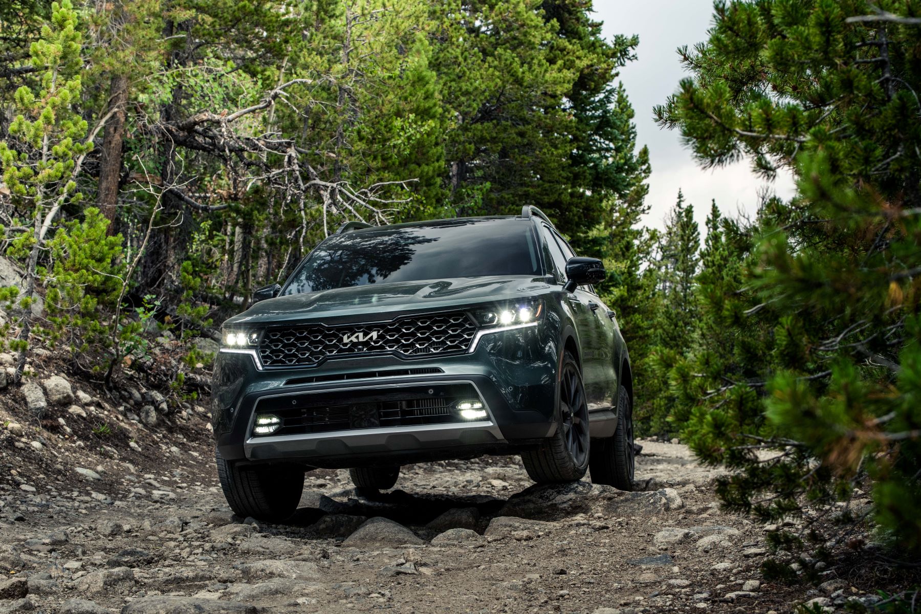 A green 2022 Kia Sorento X-Line midsize SUV model traveling off-road on a rocky gravel trail through a forest