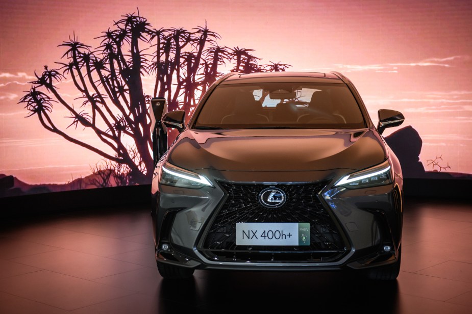 A 2022 Lexus NX parked in front of a pink backdrop with a tree silhouette. 
