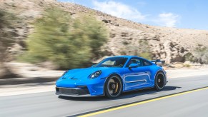 A blue 2022 Porsche 911 GT3 driving down a desert canyon road