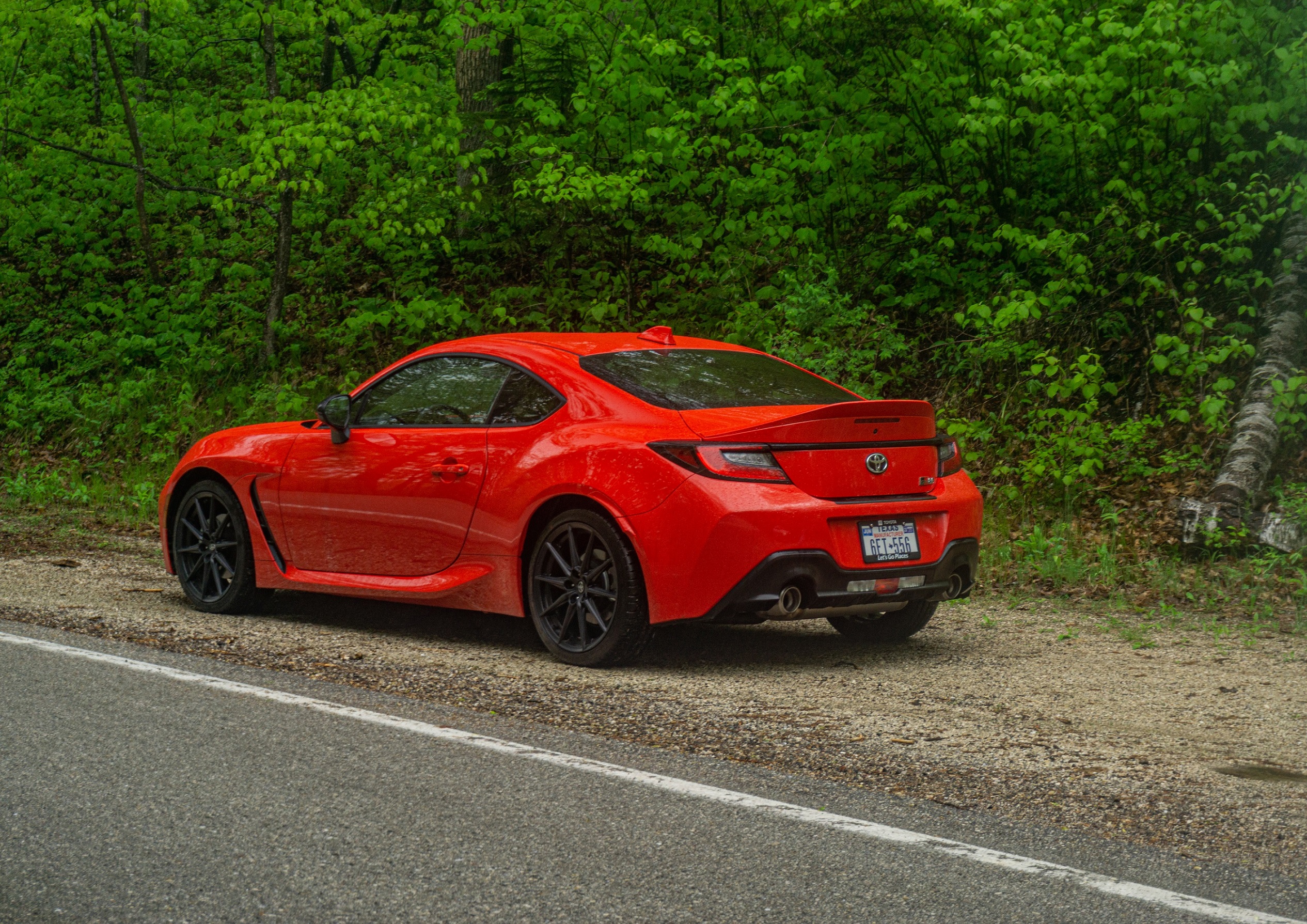 The rear 3/4 view of a red 2022 Toyota GR86 Premium on a forest road
