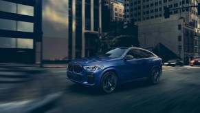 A blue 2022 BMW X6 driving through a city.