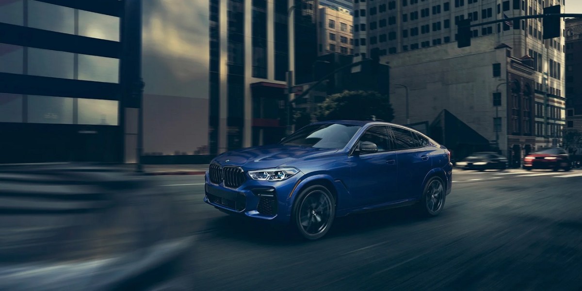 A blue 2022 BMW X6 driving through a city.