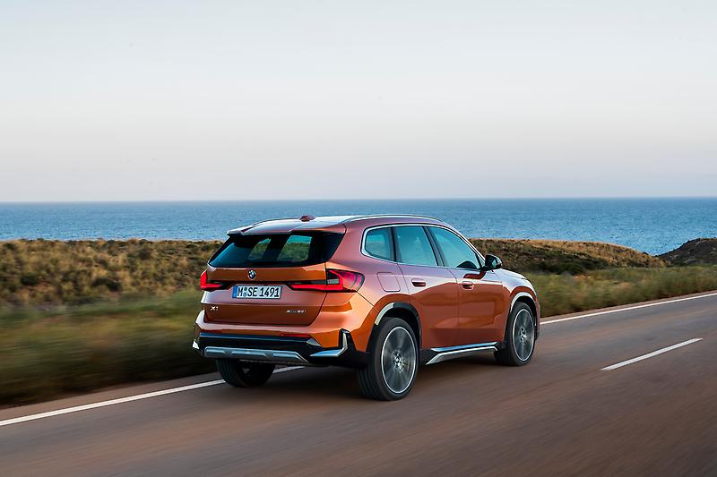 The 2023 BMW X1 in orange driving along a shore. 
