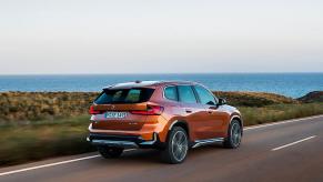 A 2023 BMW X1 in orange by the shore.
