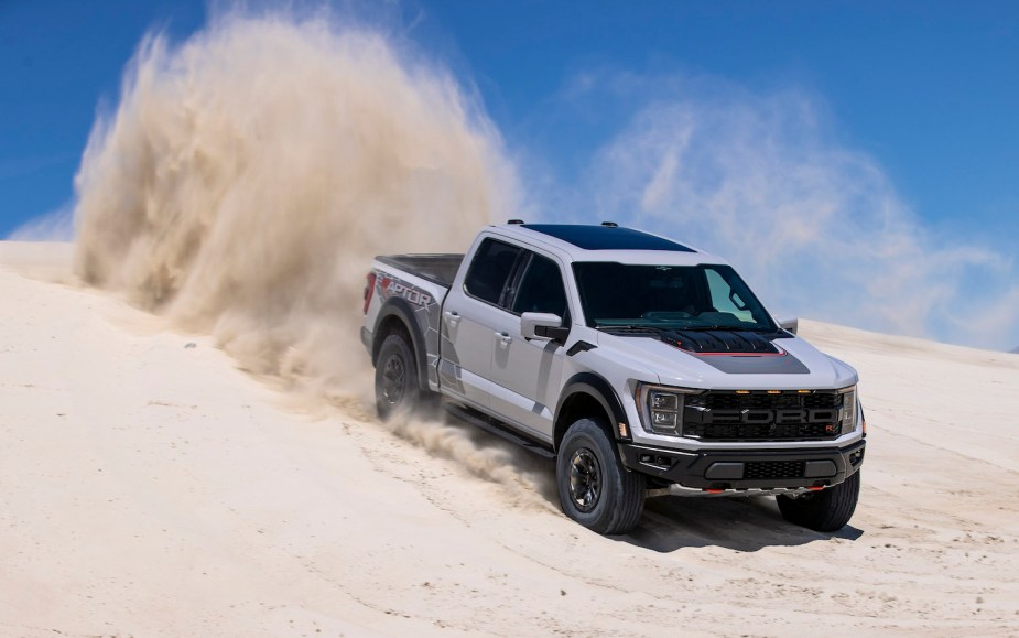 Gray Ford F-150 Raptor driving down a sand dune with a cloud of dust visible in the background.