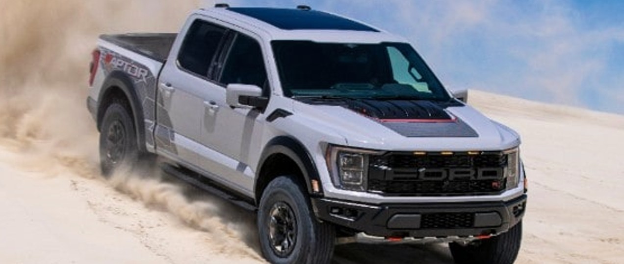 A white 2023 Ford F-150 Raptor R pickup truck is driving in the sand.