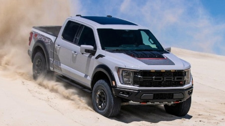 A white 2023 Ford F-150 Raptor R pickup truck is driving in the sand.