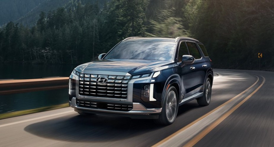 A blue 2023 Hyundai Palisade midsize SUV is driving on the road.