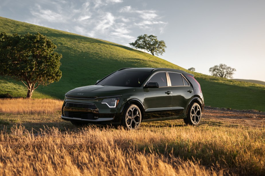 A dark color2023 Kia Niro parked in a field and mountainous area.