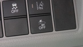 A Honda's black Electronic Stability Control Off button next to its black Lane-Keeping Assist and Emergency Braking buttons set in a gray panel