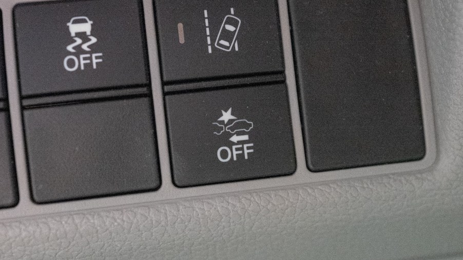 A Honda's black Electronic Stability Control Off button next to its black Lane-Keeping Assist and Emergency Braking buttons set in a gray panel