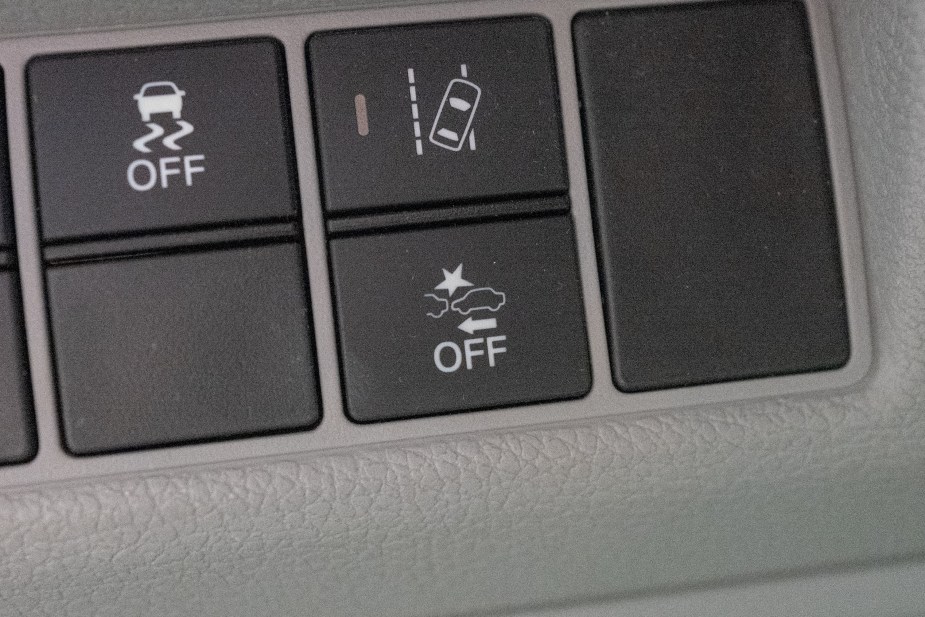 A Honda's black Electronic Stability Control Off button next to its black Lane-Keeping Assist and Emergency Braking buttons set in a gray panel