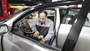 A gray-clothed car mechanic uses an OBD2 scanner to check for diagnostic trouble codes in a silver Toyota Avalon